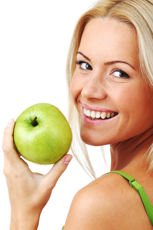 Улыбающаяся девушка блондинка с зеленым яблоком в руке на белом фоне