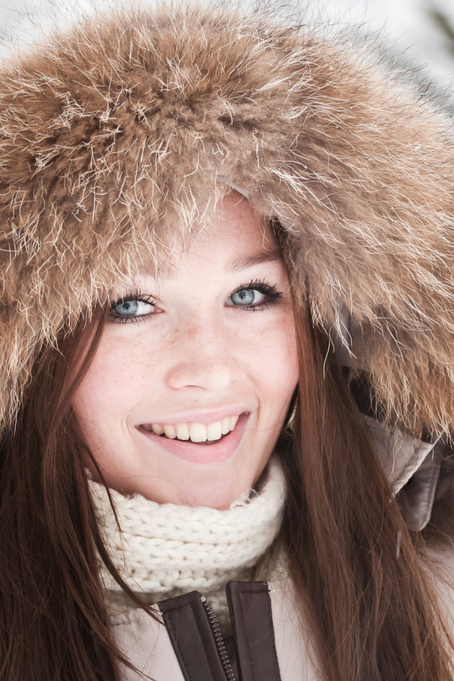 Улыбающаяся голубоглазая девушка в капюшоне зимой