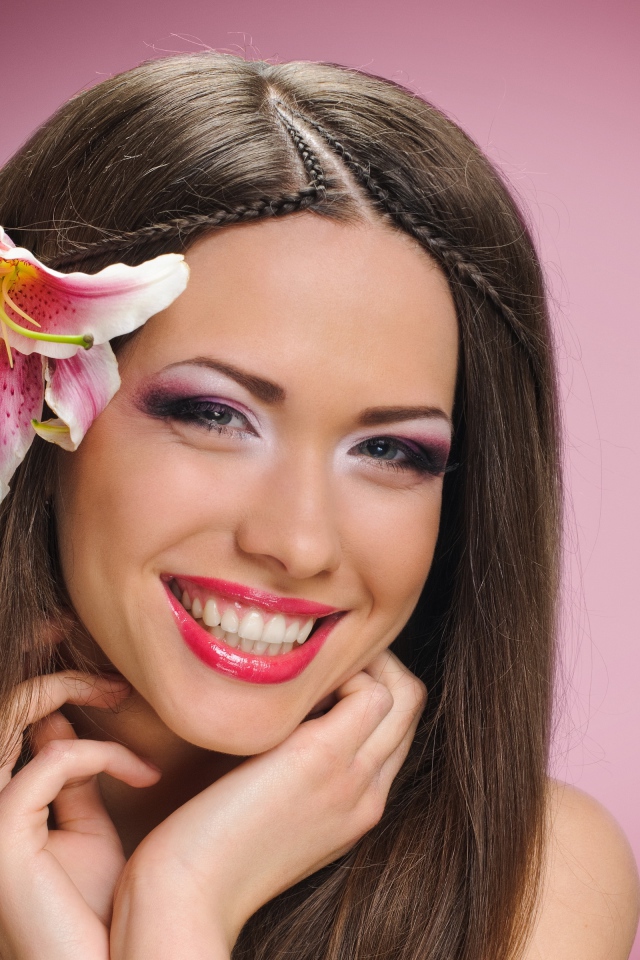 Улыбающаяся девушка с цветком лилии в волосах на розовом фоне 