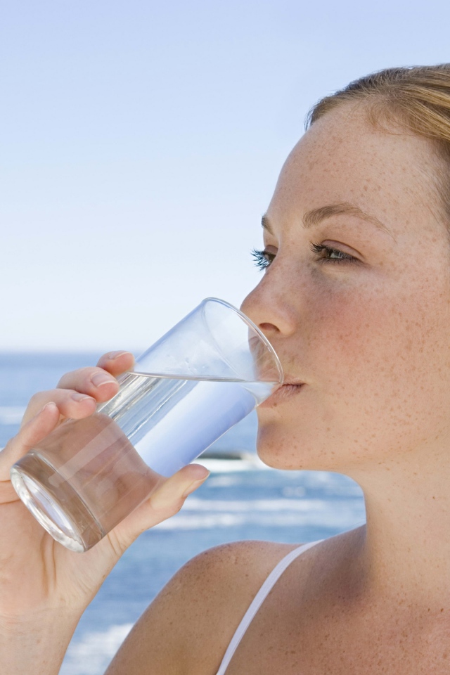 Девушка пьет воду со стакана на фоне моря