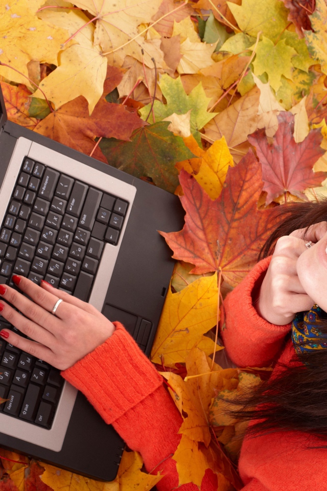 Девушка лежит на сухой опавшей листве с ноутбуком осенью