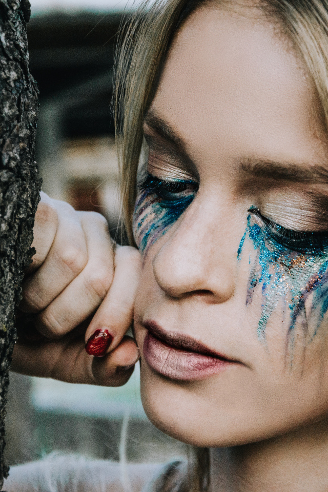 Заплаканная блондинка стоит у дерева