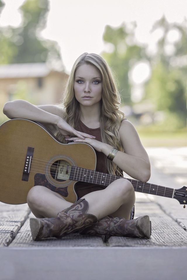 Молодая девушка блондинка сидит на мосту с гитарой