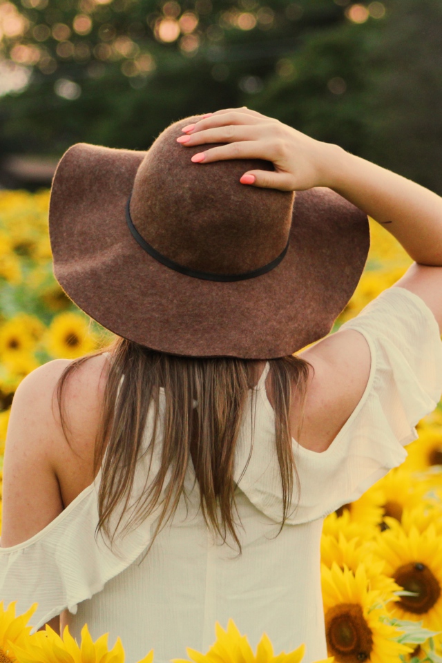 Молодая девушка в большой шляпе на поле с подсолнухами 