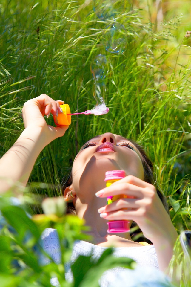 Молодая девушка лежит на зеленой траве с мыльными пузырями