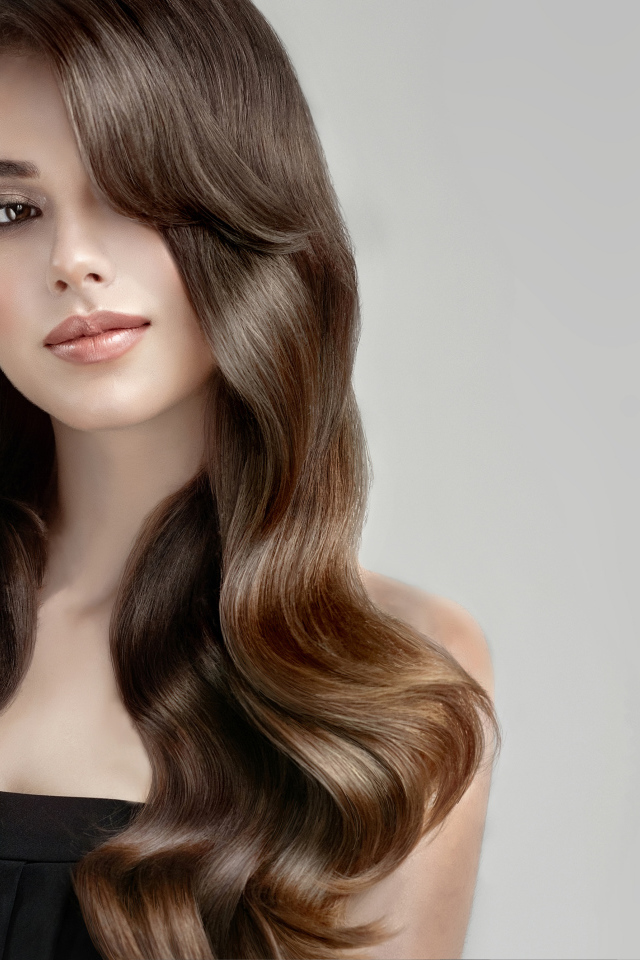 Молодая девушка с красивыми длинными волосами на сером фоне