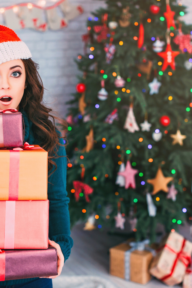 Удивленная девушка с подарками у новогодней елки 