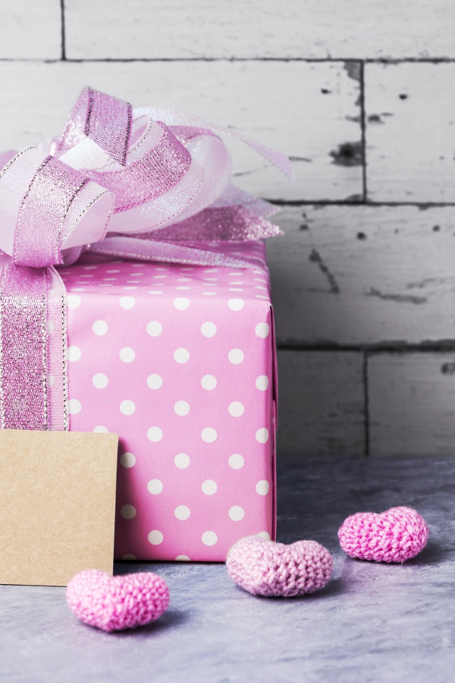 Большая сиреневая подарочная коробка с бантом и маленькими сердечками на фоне стены