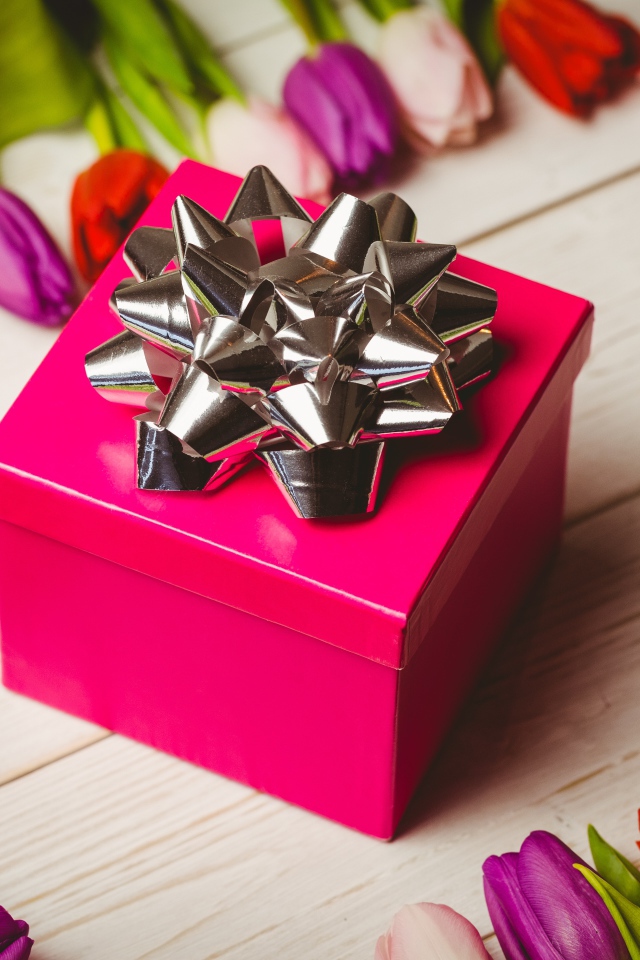 Красная коробка с подарком на столе с тюльпанами