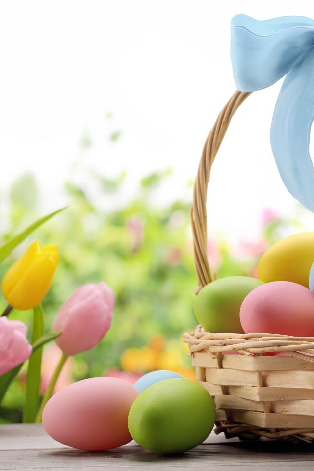 Корзина крашеных яиц с голубым бантом  на фоне тюльпанов на  Пасху