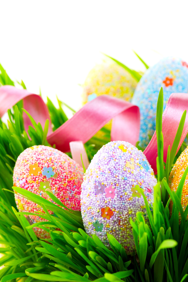 Пасхальные яйца в зеленой траве с розовой лентой на белом фоне
