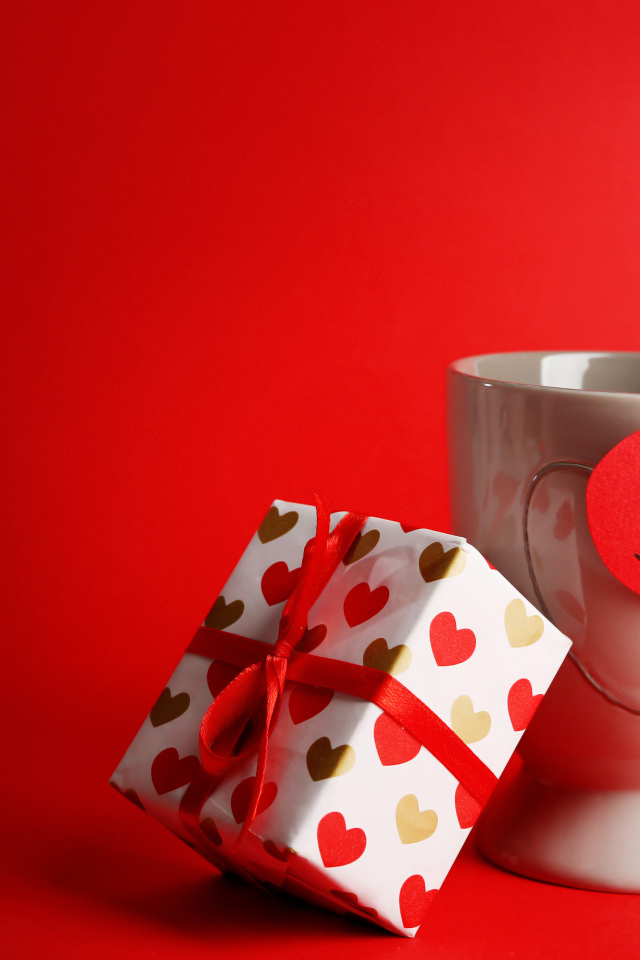 Чашка с подарком и валентинкой на красном фоне на 14 февраля