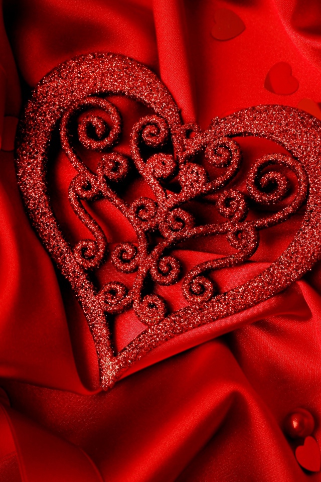 Блестящее сердце на красной атласной ткани 