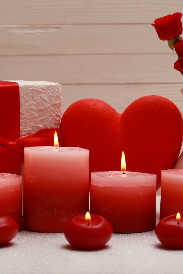 Lighted red candles on the table with a gift, red heart and flowers in a vase