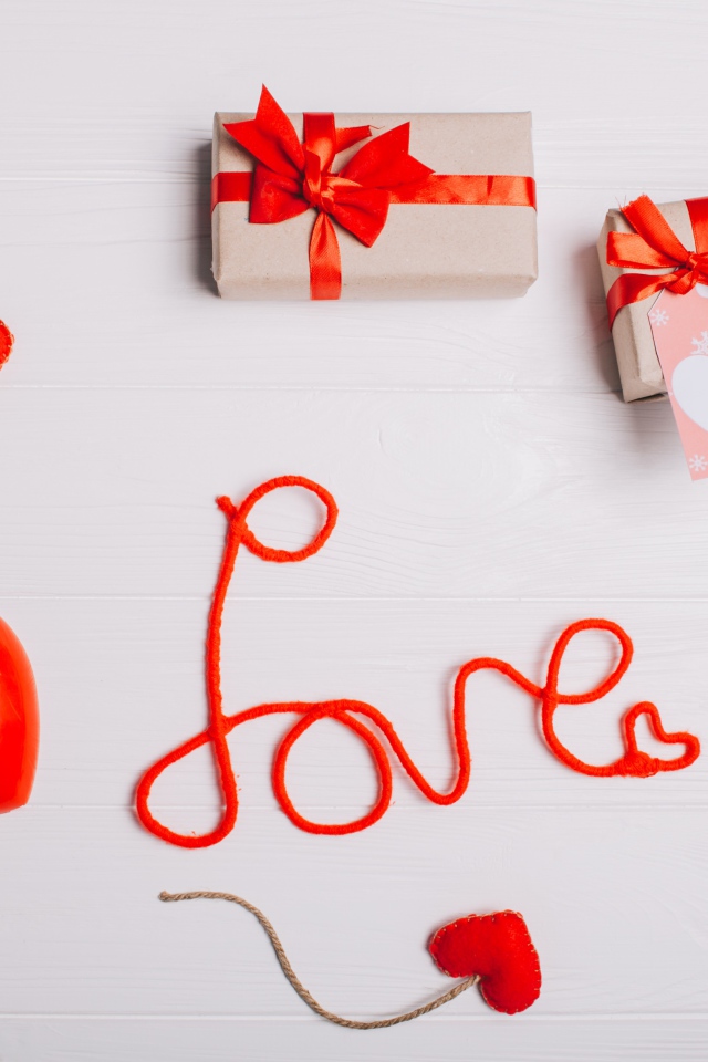 Надпись любовь красными нитями на сером фоне с сердечками и подарками