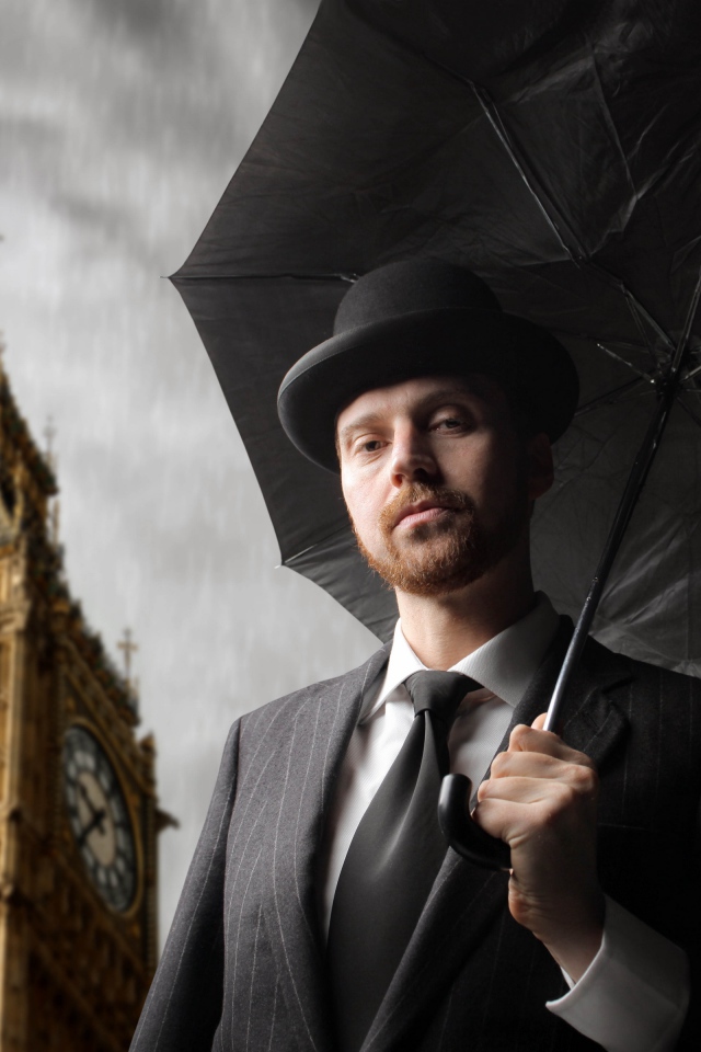 Мужчина в костюме с черным зонтом у башни с часами 