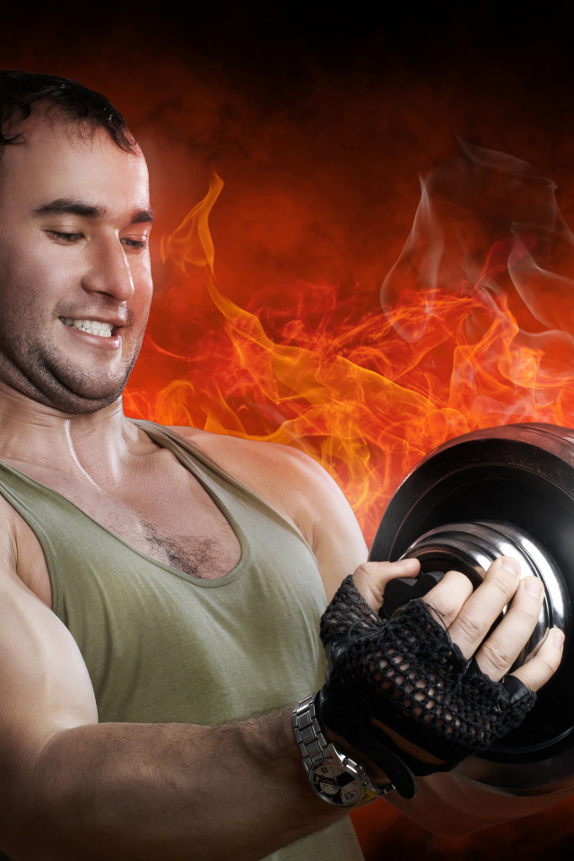 Мужчина спортсмен держит в руках гантелю на фоне огня