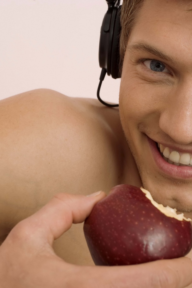Handsome blue-eyed guy in headphones with an apple in his hand