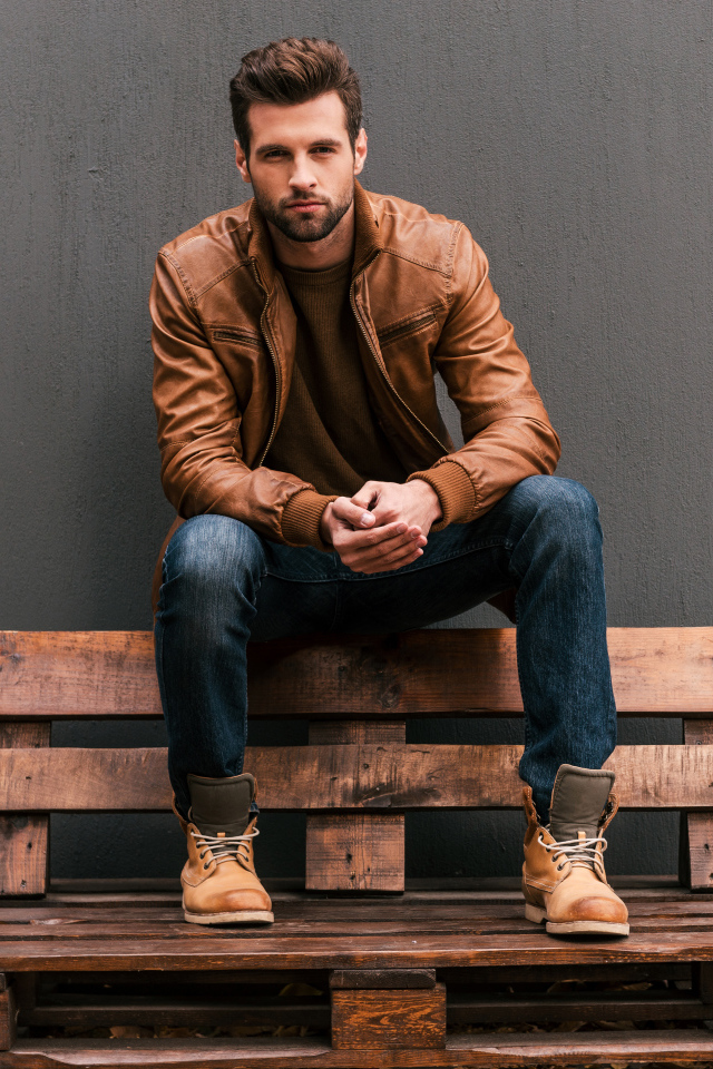 Молодой красивый мужчина сидит на деревянной лавке