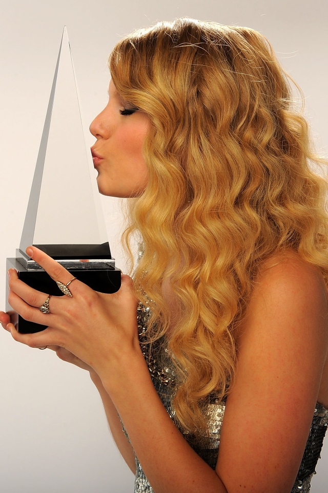 Певица Тейлор Свифт целует награду на сером фоне