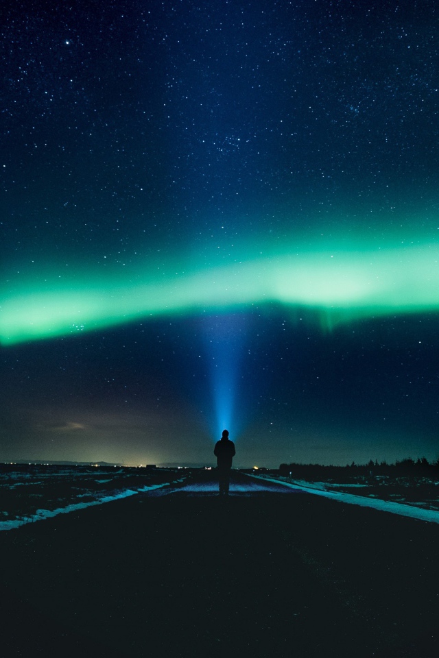 Человек идет по дороге ночью на фоне северного сияния