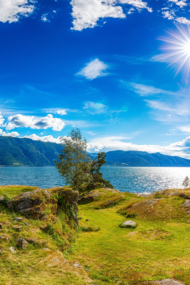 Красивое яркое солнце в голубом небе над горами и водой, Исландия