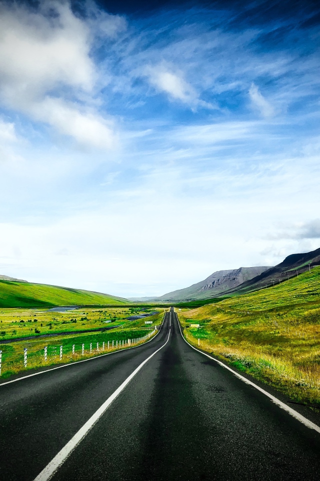 Ровная дорога у зеленых холмов на фоне голубого неба