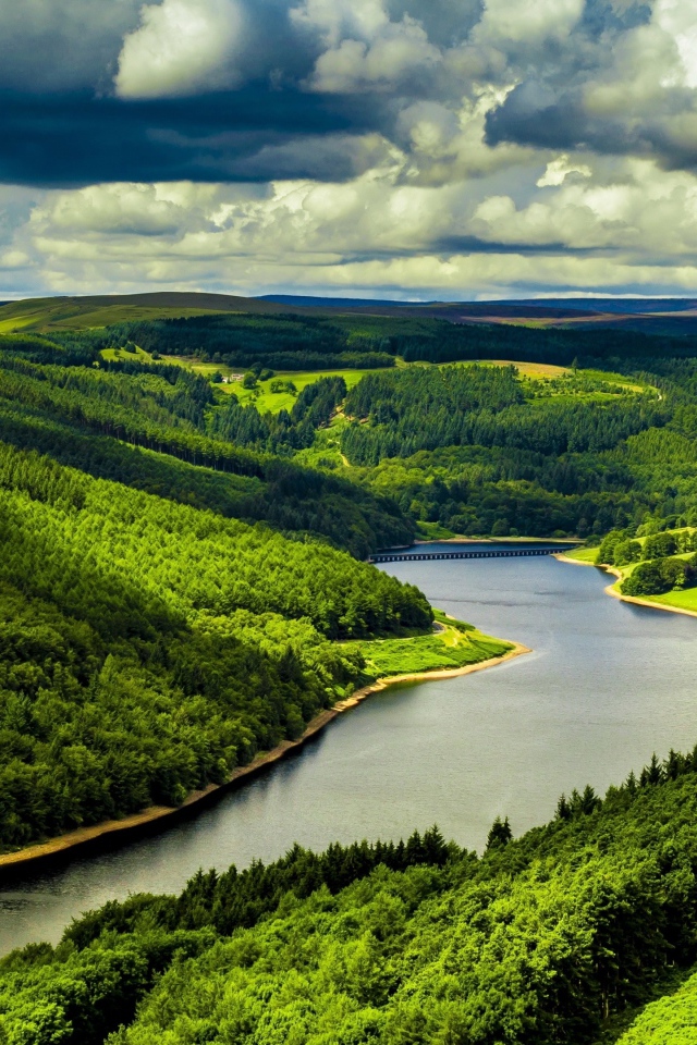 Зеленые холмы у реки под небом с густыми белыми облаками