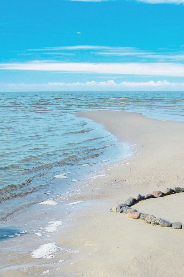 Сердце из камней на песке у спокойного моря под голубым небом
