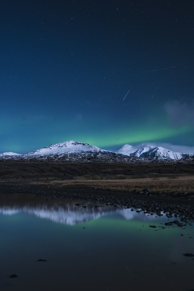 Горы и небо отражаются в луже на дороге ночью 