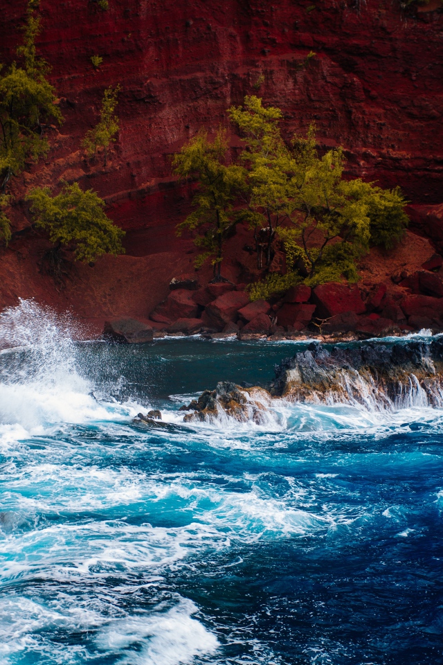 Грубое море брызгает камнями перед красным песчаным океанским заливом в Хане