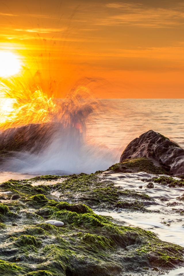 Бушующие волны в море бьются об камни на закате