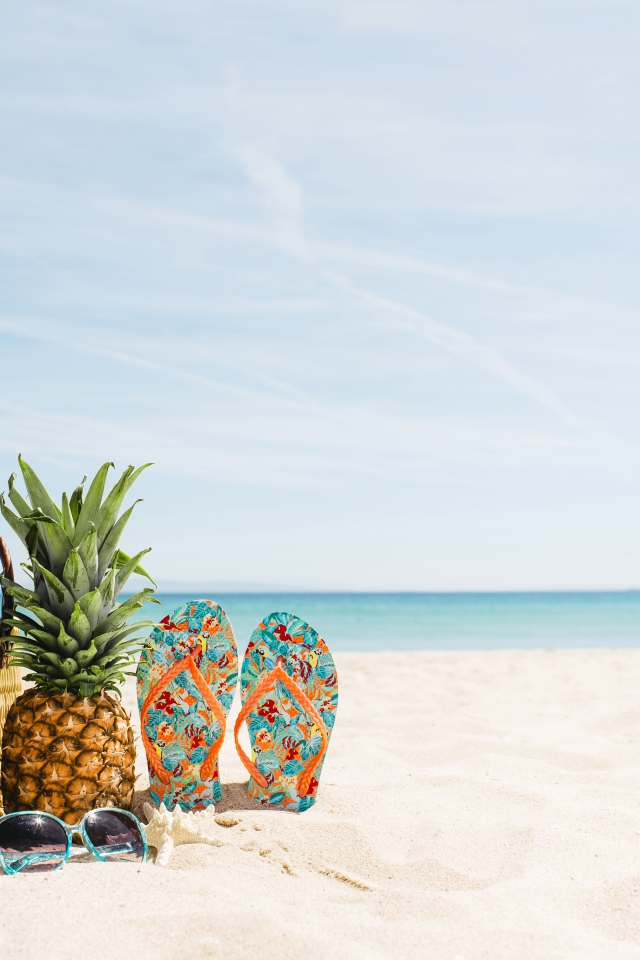 Сумка, ананас, шлепанцы и солнечные очки лежат на песке на пляже летом