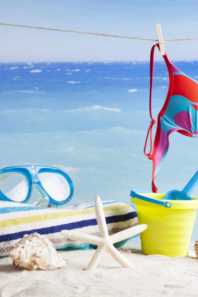 Очки, купальник, полотенце, ракушки и игрушки на песке на пляже летом