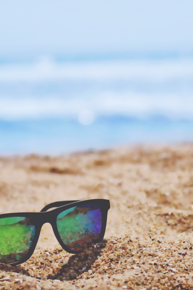 Солнцезащитные очки лежат на желтом песке у моря