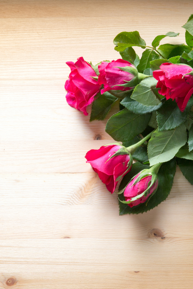 Букет розовых роз с зелеными листьями на деревянной поверхности 