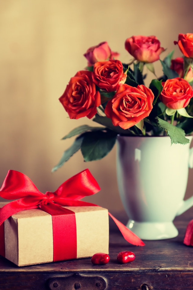 Букет роз в белой вазе с подарком на столе