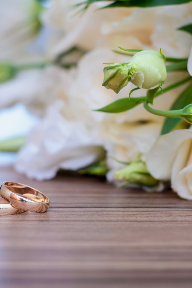 Букет белых роз на столе с золотыми обручальными кольцами