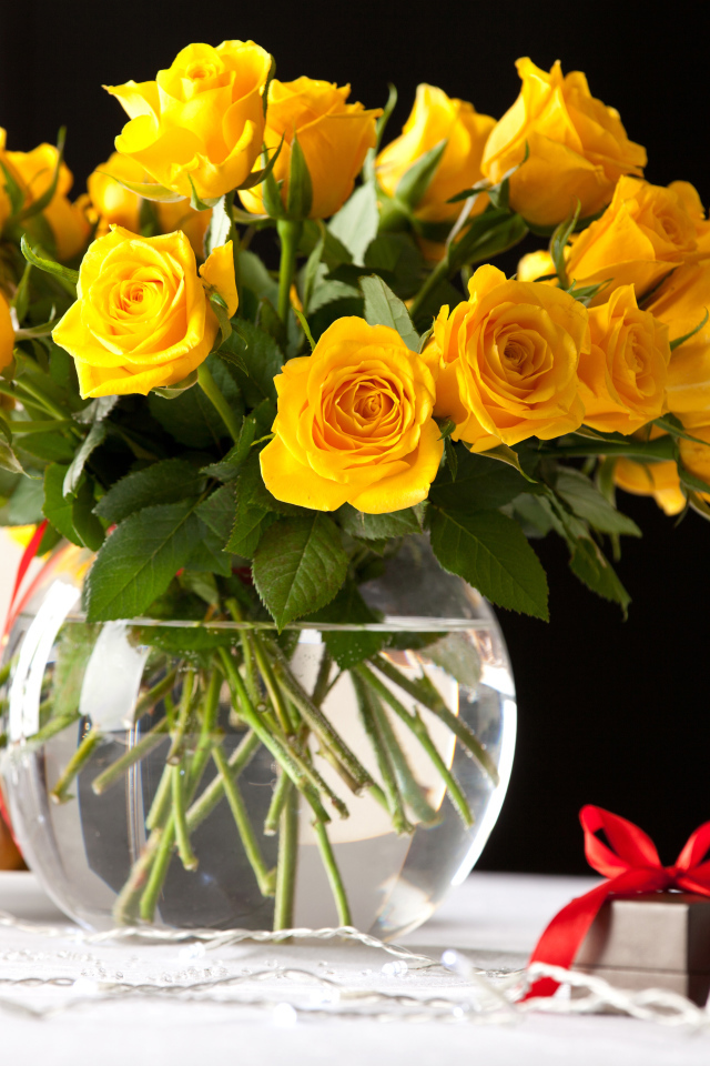 Букет желтых роз в стеклянной вазе с бокалами шампанского на столе