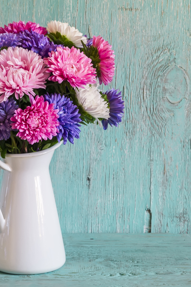 Разноцветные астры в вазе на деревянном фоне