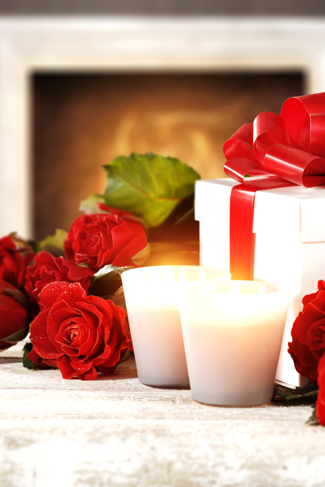 Красные розы с подарком и двумя зажженными свечами на столе