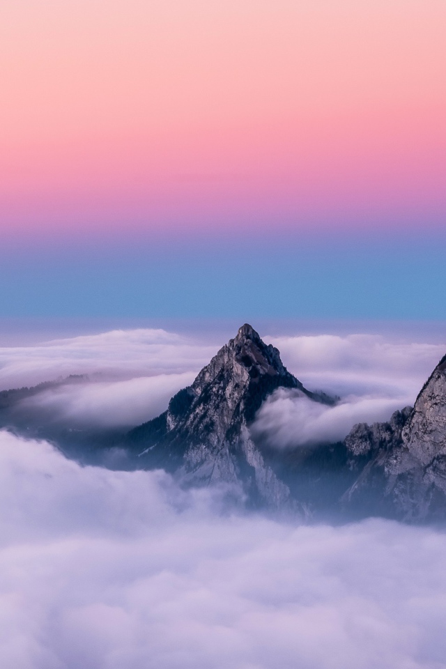 Верхушки гор в белых облаках под красивым розовым небом 