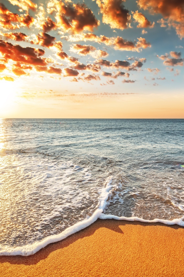 Морская волна омывает песок на берегу под красивым небом