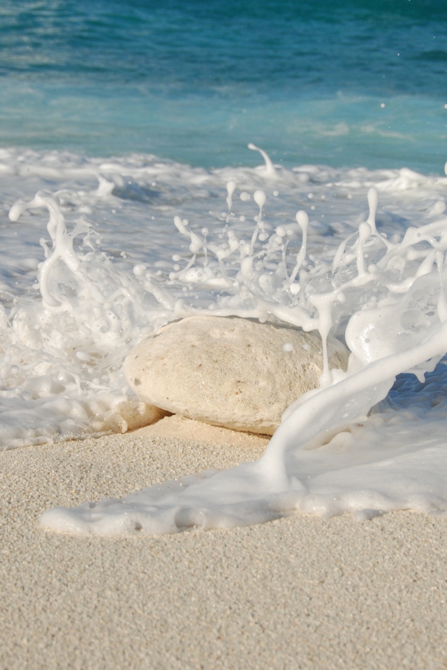 Белые морские волны бьются об камень на желтом песке