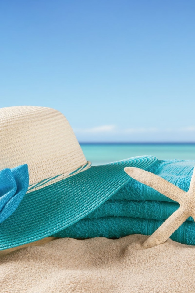 Большая шляпа, голубое полотенце и морская звезда на песке летом