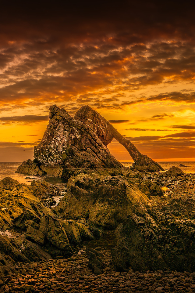Скала в море на закате солнца под облачным небом