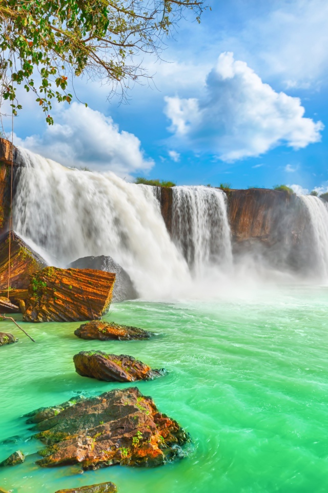 Быстрый водопад стекает со скалы под красивым голубым небом