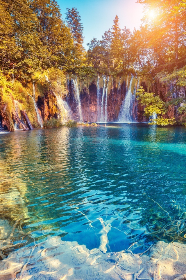 Водопад в лучах солнца стекает со скалы в реку