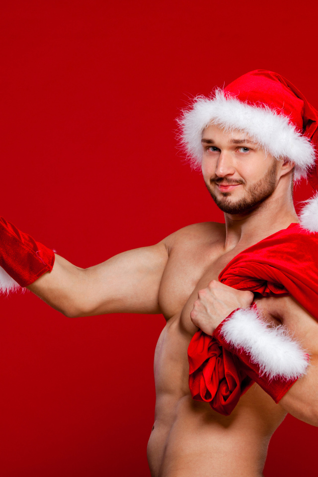 Мужчина в новогоднем костюме Санта Клауса с мешком и подарком в руке на красном фоне