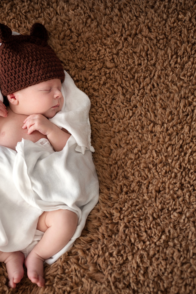Грудной ребенок в вязаной шапке  спит в белом покрывале 